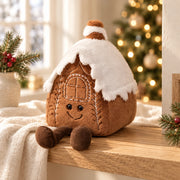 Maison en pain d’épices en peluche, toit enneigé et petites jambes brunes, dans une ambiance de Noël
