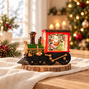 Train de Noël lumineux rouge, vert et doré avec scène de Père Noël, posé sur du lin ivoire